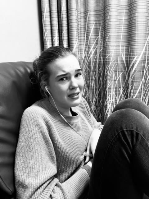 Black and white photograph of a teenage girl who is crying while she is sitting on a chair with her legs hunched up.