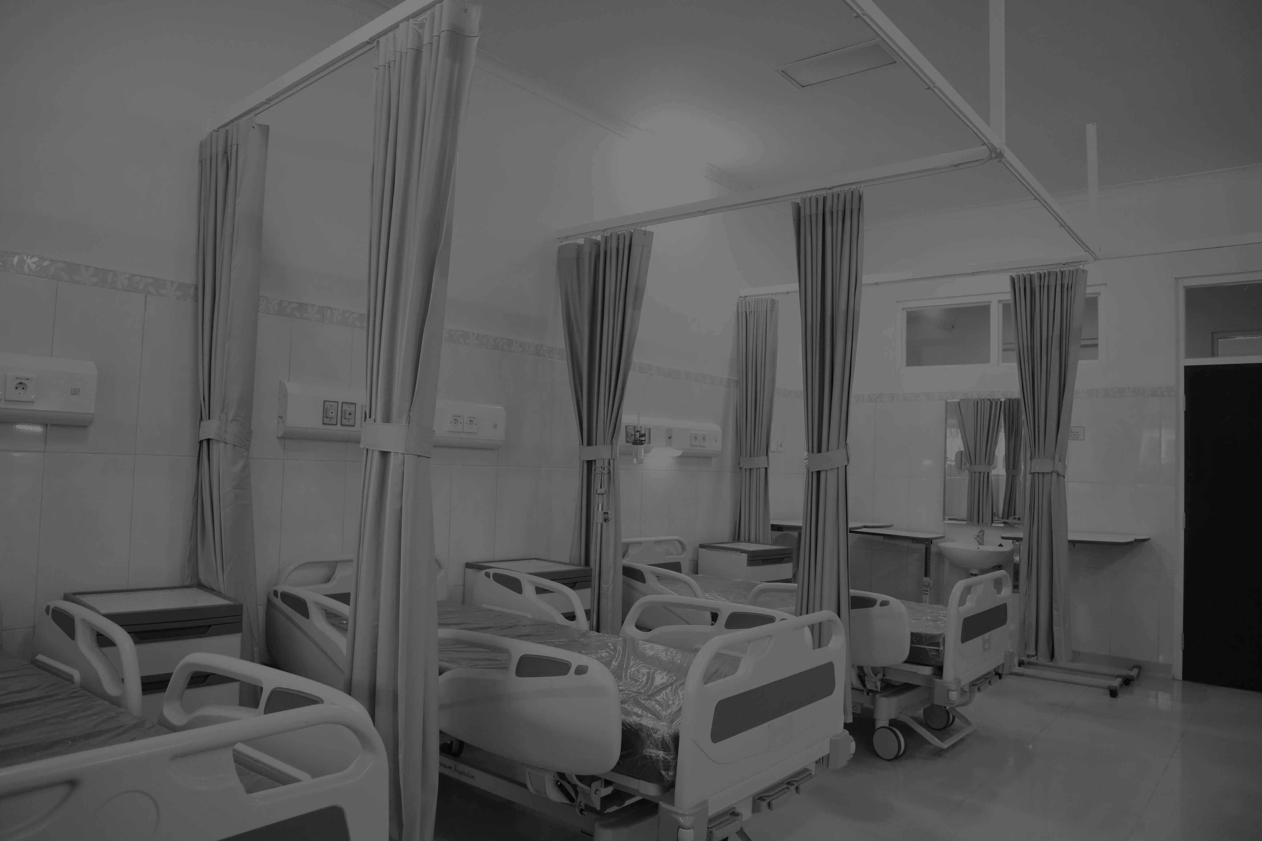 Photograph of a hospital ward with empty hospital beds and curtain dividers.
